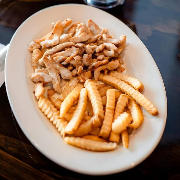 A white oval plate holds golden crinkle-cut fries and chicken strips drizzled with white sauce.