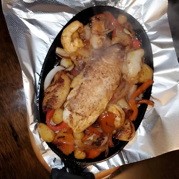 Steaming hot seafood fajitas with fish, shrimp, onions, and peppers in a sizzling skillet.