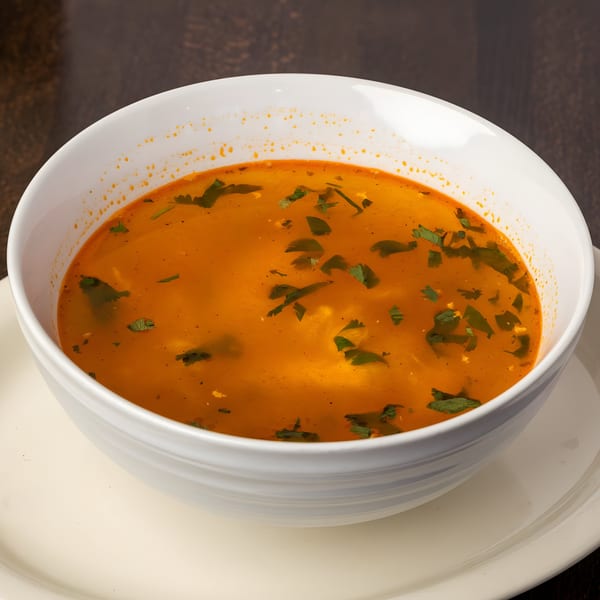 A white bowl filled with a vibrant orange Mexican soup, garnished with fresh green herbs.